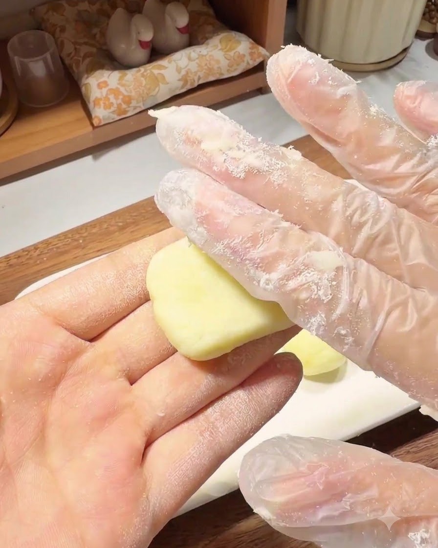 A gloved hand pressing a small ball of potato dough into a flat, round pancake shape in the palm of the hand.