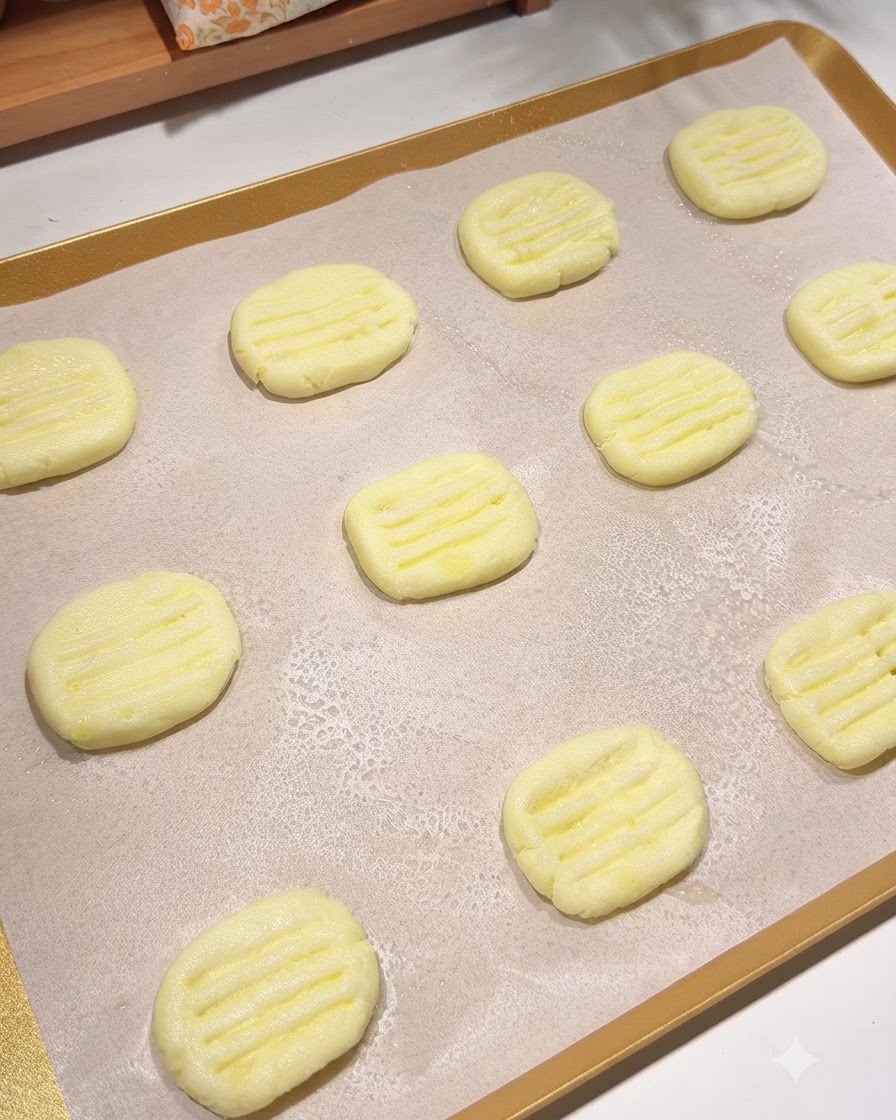 A baking tray lined with parchment paper holding multiple shaped potato pancakes with a fine mist of cooking oil sprayed over them.