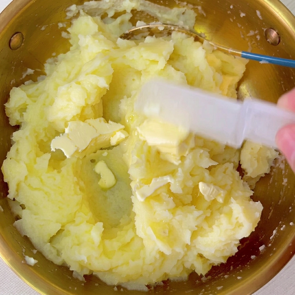 Pieces of butter being mixed into the bowl of warm mashed potatoes.