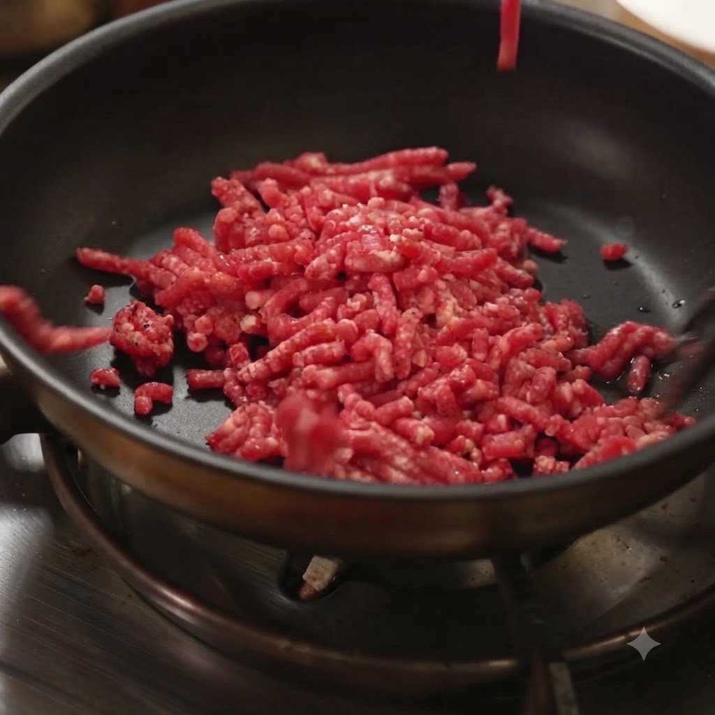 Raw minced meat being added to a hot black frying pan on a stove.
