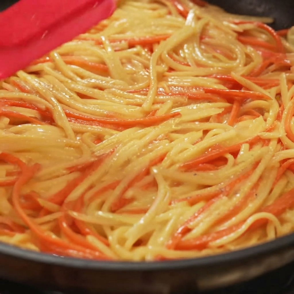 A spatula spreading and flattening a potato and carrot mixture evenly in a frying pan.