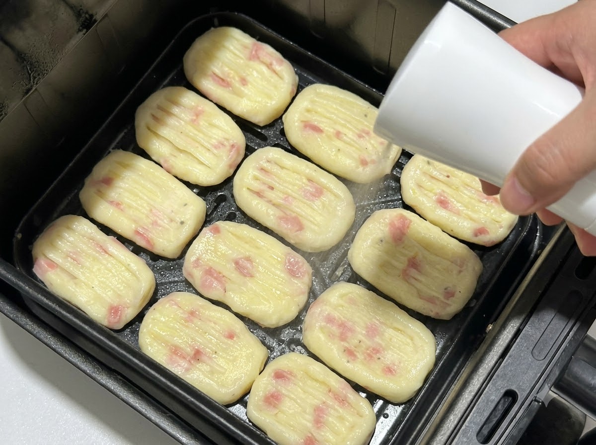 Shaped potato patties arranged in an air fryer basket while being sprayed with oil from a spray bottle.