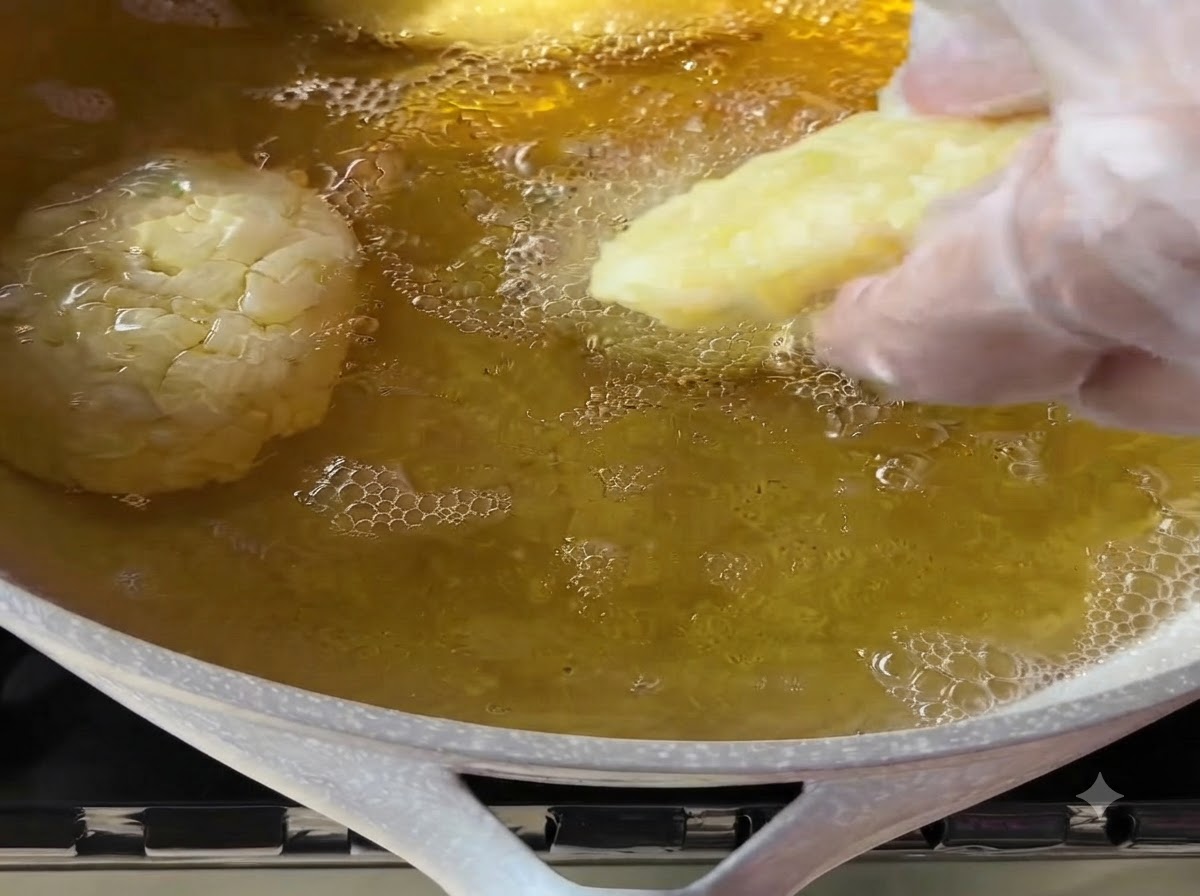 A gloved hand gently placing a shaped potato patty into a pan of hot bubbling cooking oil.