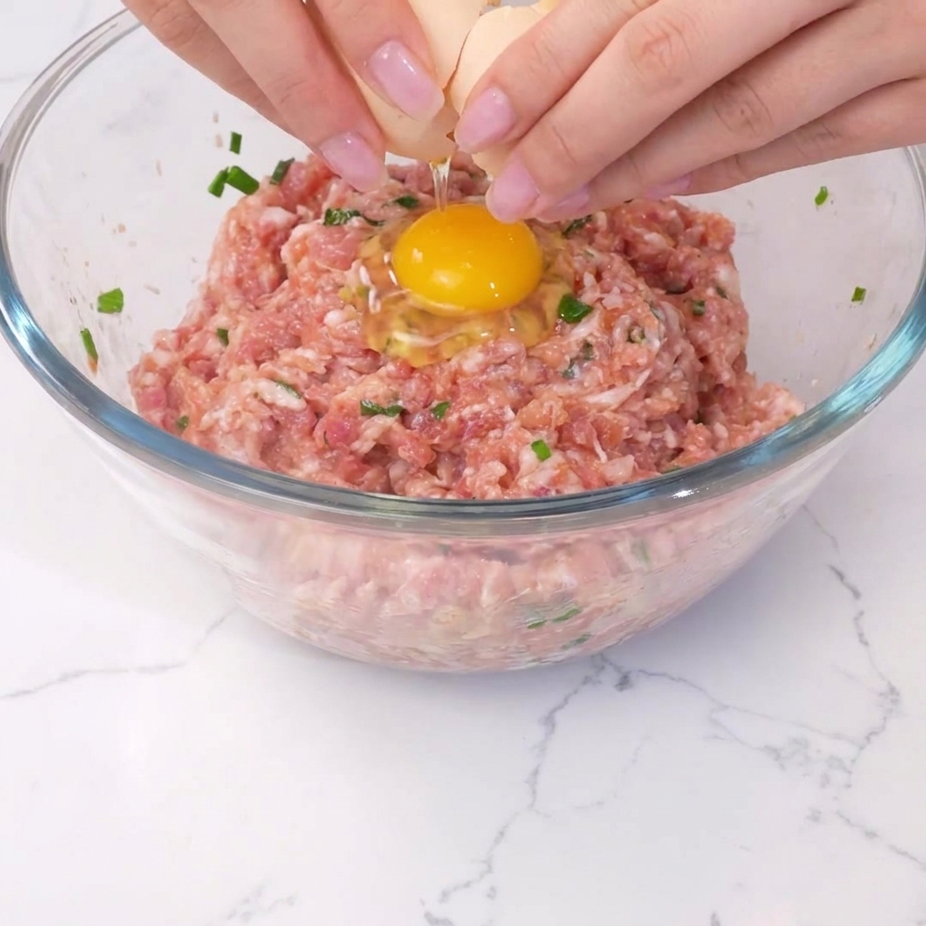 An egg being cracked into the center of the seasoned meat mixture.