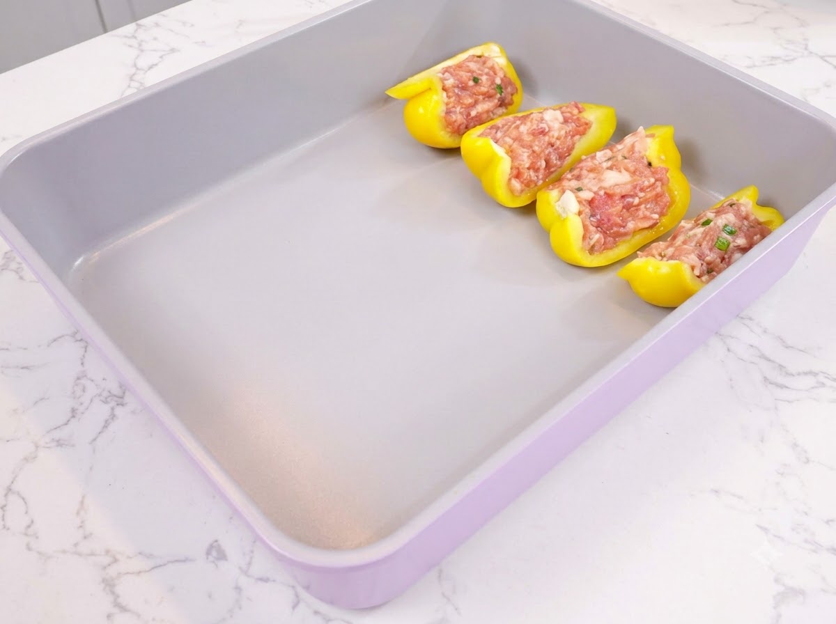 Yellow bell pepper halves stuffed with seasoned minced meat neatly arranged in a purple baking tray.