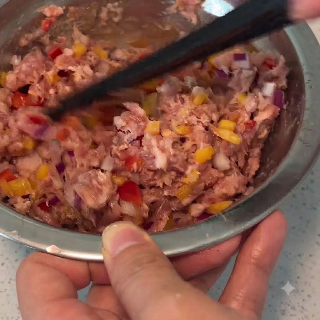 A pair of chopsticks mixing minced pork, vegetables, and seasonings together inside a metal bowl.