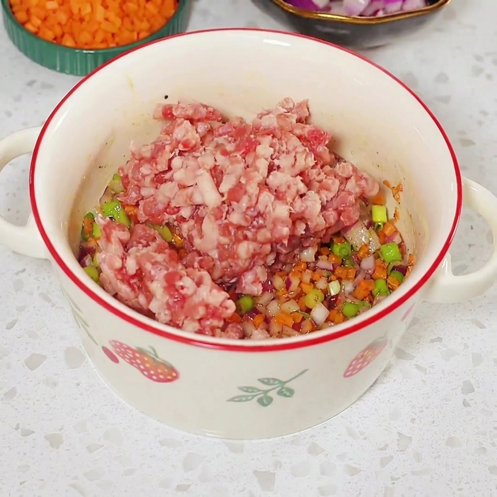 Raw minced meat placed on top of the seasoned vegetable mixture inside a white bowl.