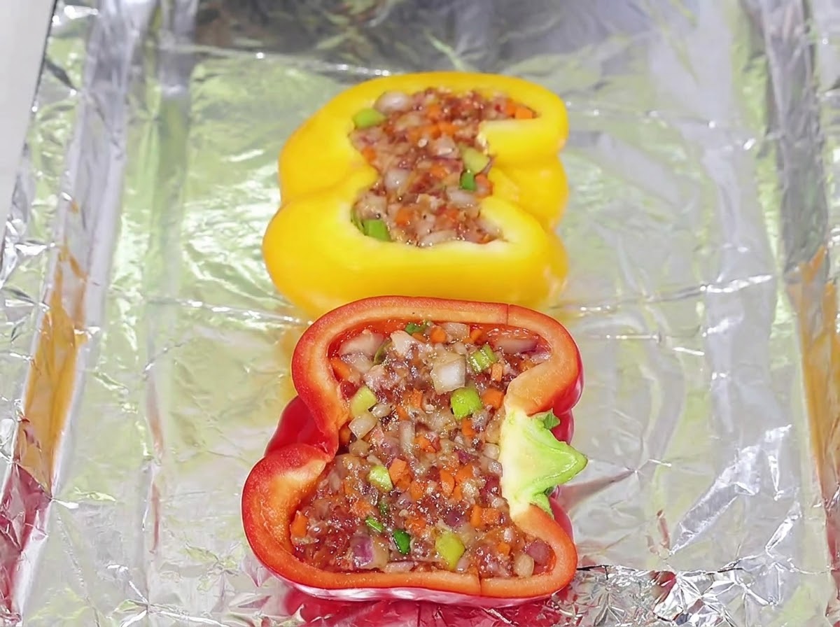 Stuffed yellow and red bell pepper halves filled with meat mixture arranged on a foil-lined baking tray.