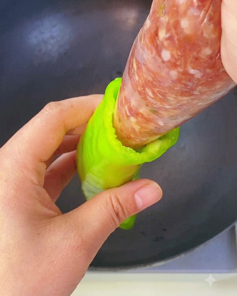 A hand squeezing seasoned meat filling from a piping bag directly into the cavity of a green pepper.