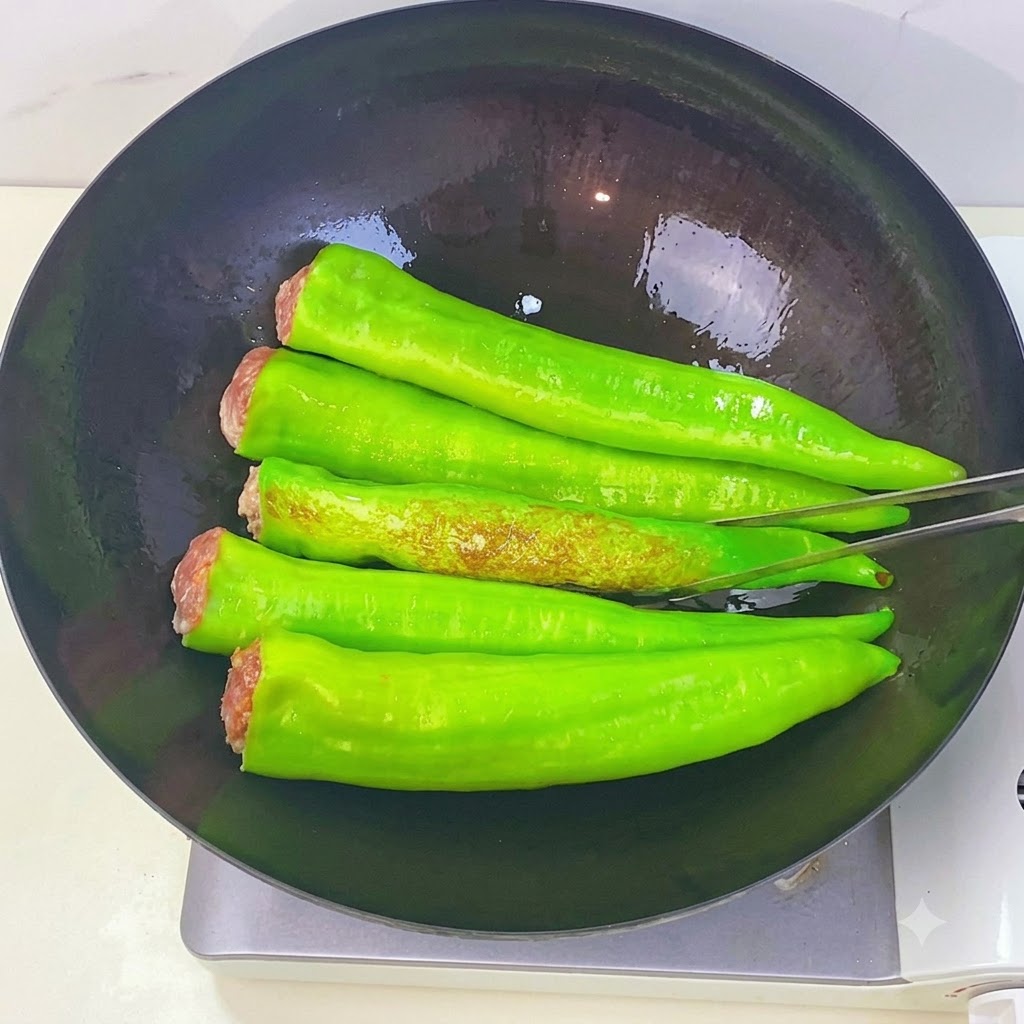 Green peppers frying in a wok showing browned tiger skin spots as they are being flipped with kitchen tongs.