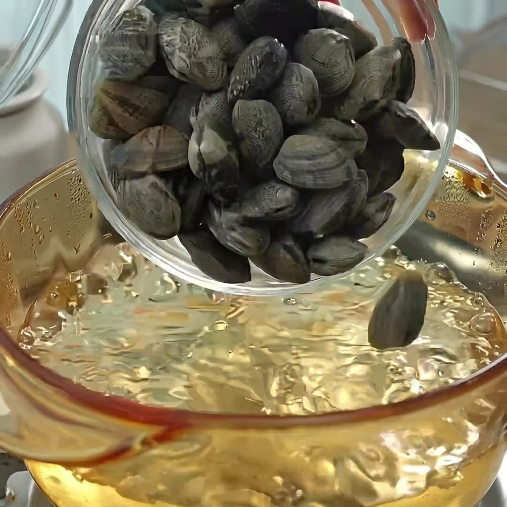 Clams being poured into a pot of boiling water to cook and make broth.
