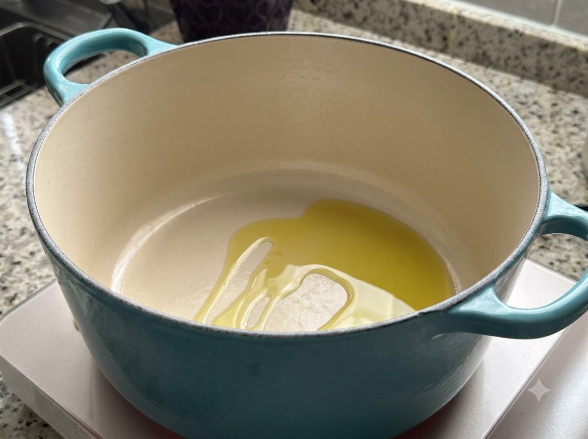 A teal Dutch oven on a stovetop with a pool of olive oil heating inside.