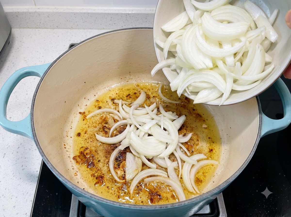 Sliced onions being poured from a small bowl into a pot containing sautéed garlic and oil.