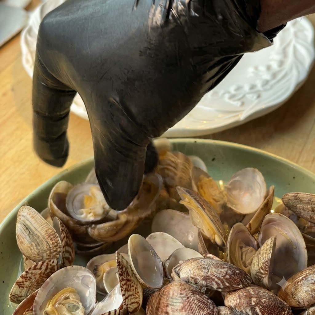 A person wearing a black glove picking clam meat out of shells into a plate.