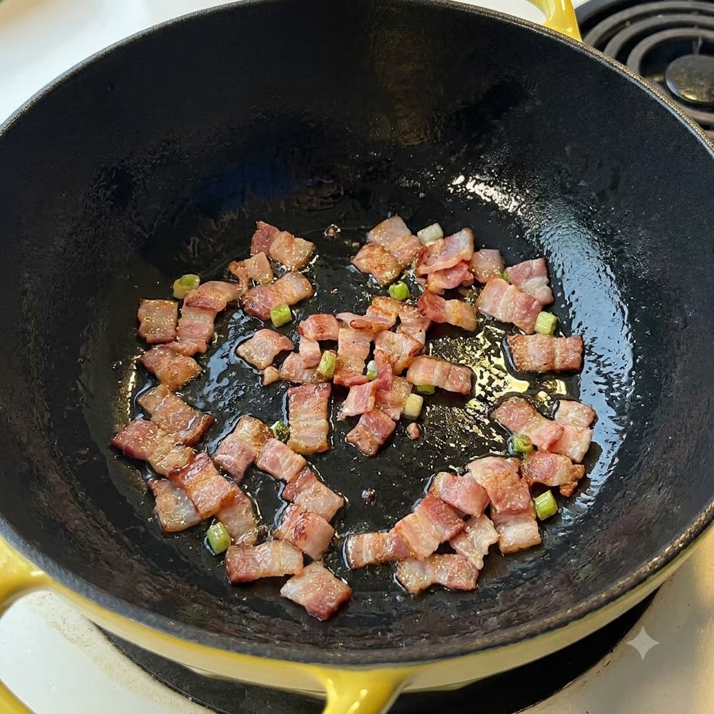 Bacon pieces sizzling and frying in a dark pan.