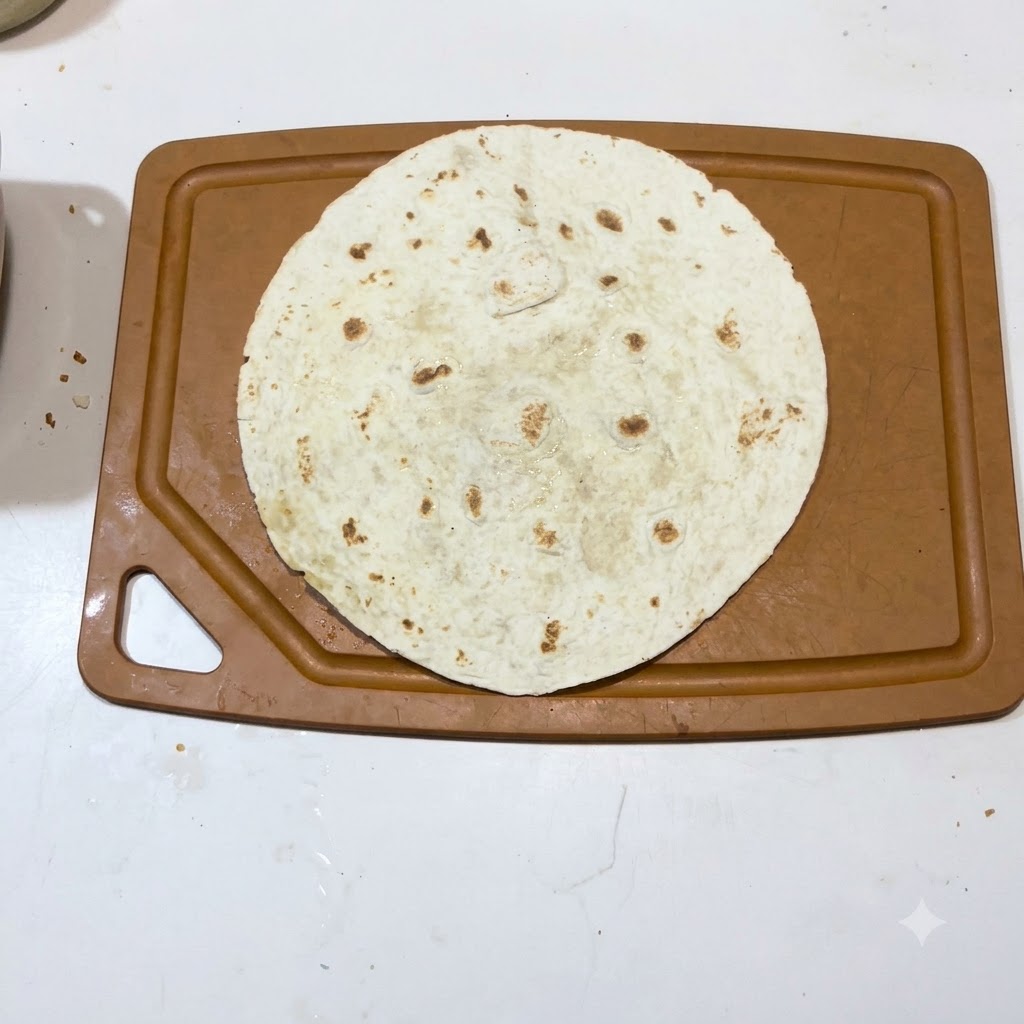 A single warm tortilla laid flat on a brown cutting board surface.