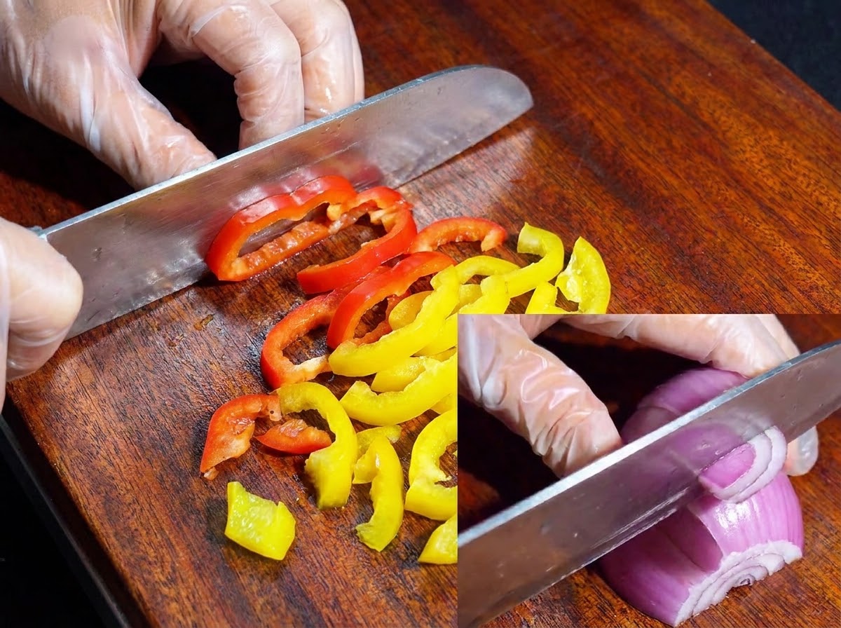 A knife slicing colorful bell peppers and red onion on a wooden cutting board.