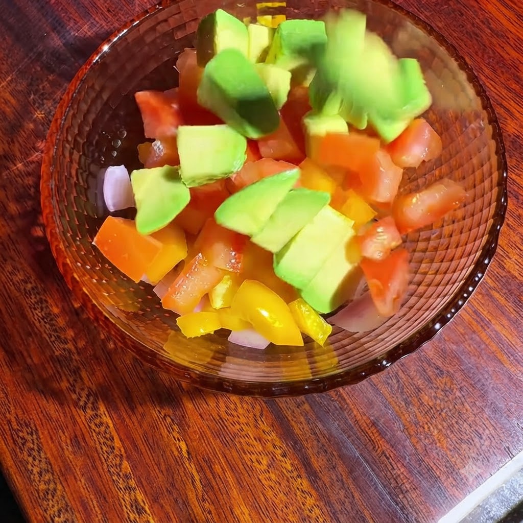 A bowl of diced vegetables and avocado being tossed and seasoned with oil and lemon juice.