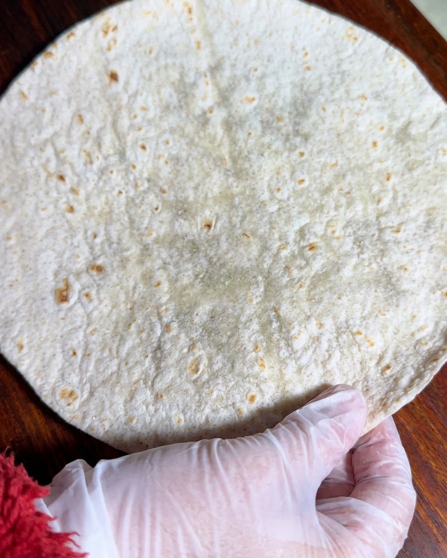 A whole wheat tortilla laid out flat on a wooden surface.