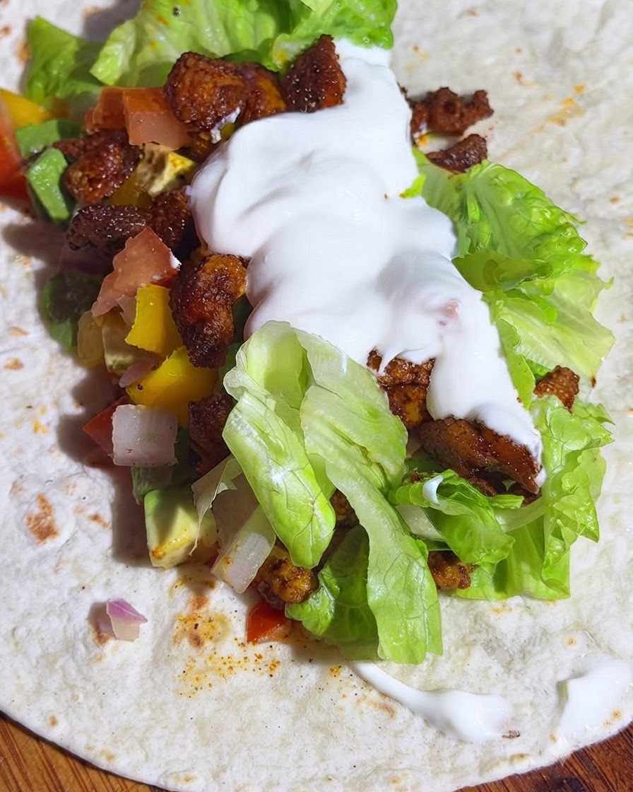 A whole wheat tortilla layered with lettuce, avocado salsa, chicken, and a dollop of yogurt.