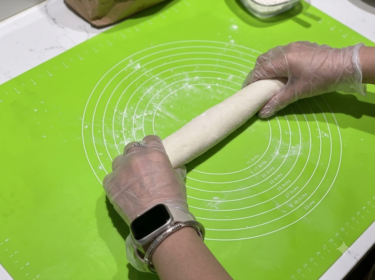 Hands rolling a dough log on a green silicone mat with measurement circles.