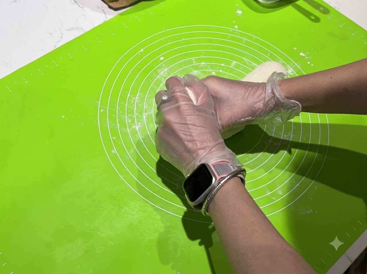 Hands dividing a long strip of dough into smaller individual pieces on a green mat.