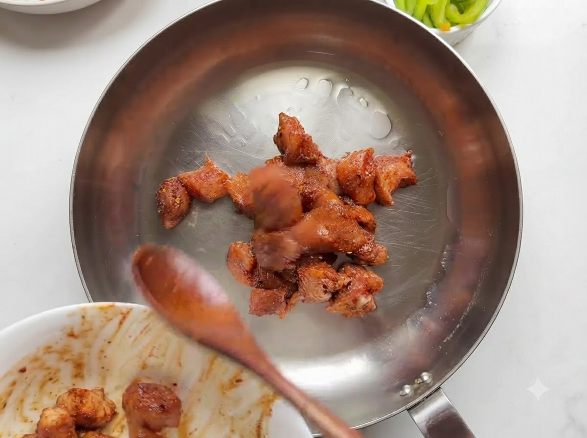 Marinated chicken pieces cooking and browning in a stainless steel skillet.