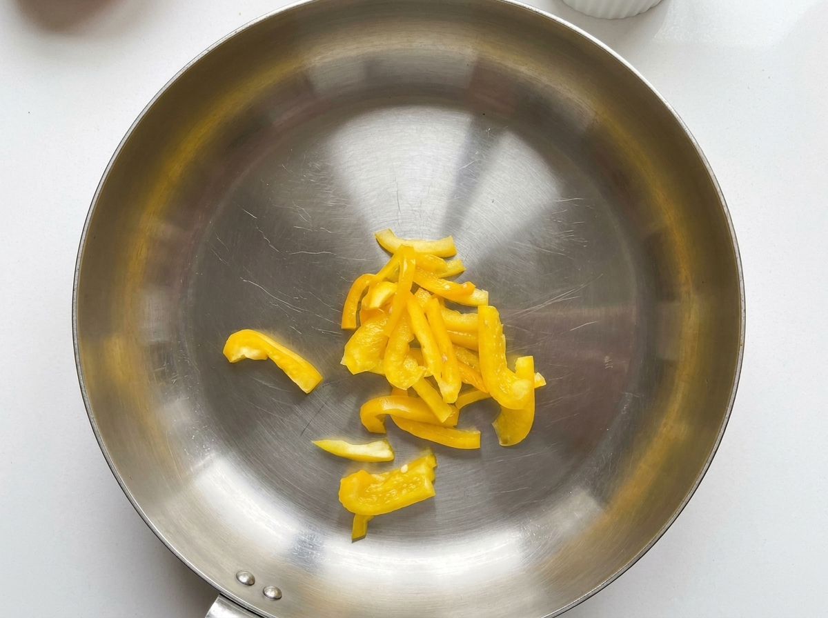 Sliced yellow bell peppers sitting in the center of a stainless steel pan.
