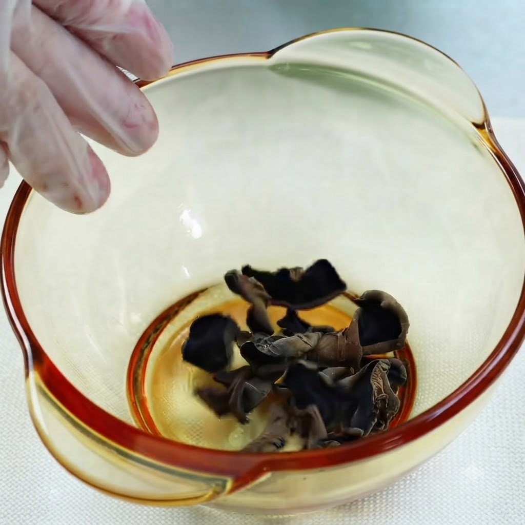 Water being poured from a glass measuring cup into a bowl of dried black wood ear mushrooms.