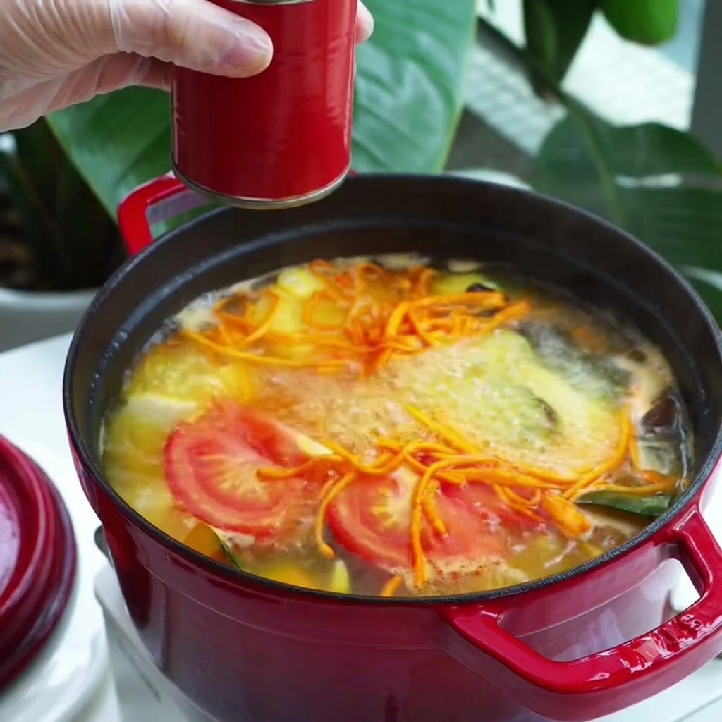 A spoonful of red paste seasoning being added into a boiling vegetable soup pot.