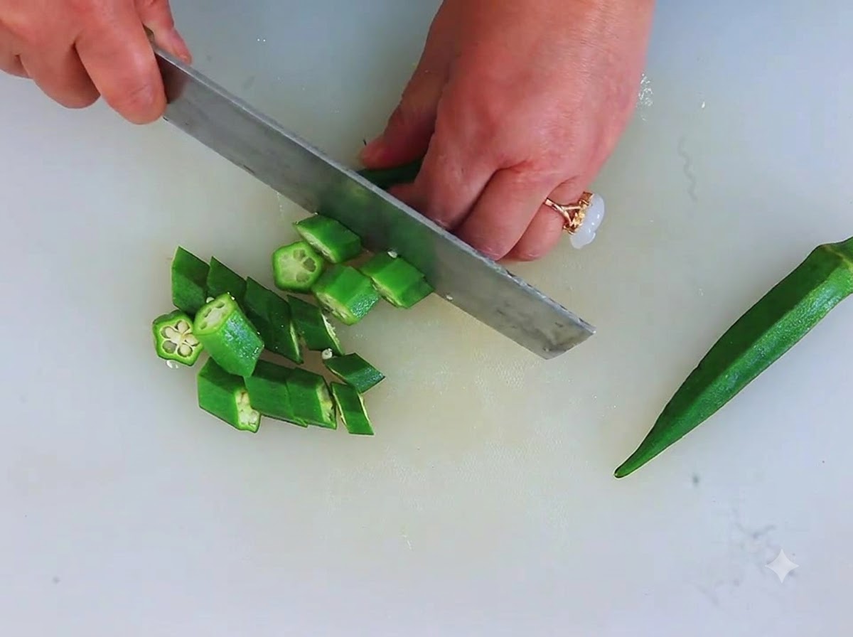 Fresh green okra being chopped into small circular star-like pieces on a cutting board.
