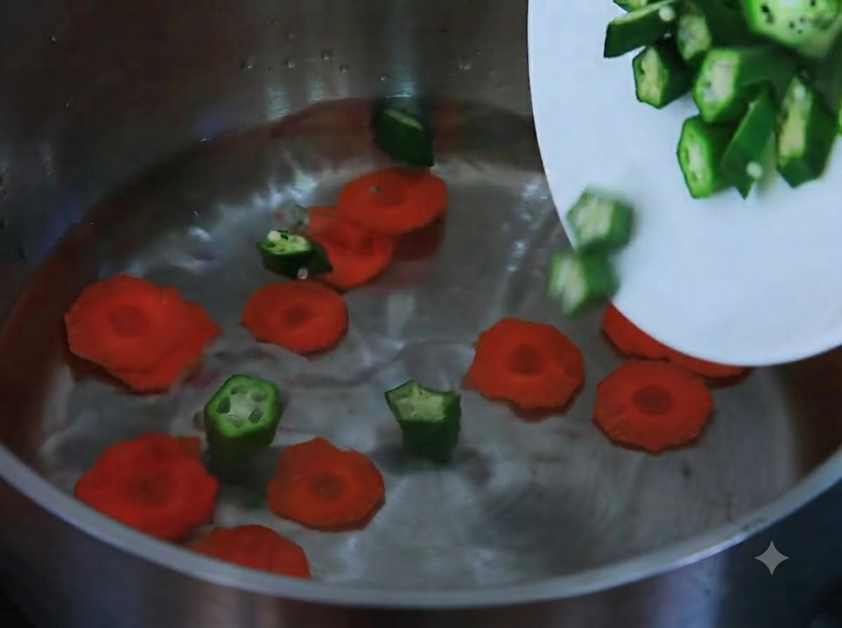 Sliced carrots and chopped okra sliding from a white plate into a pot filled with water.