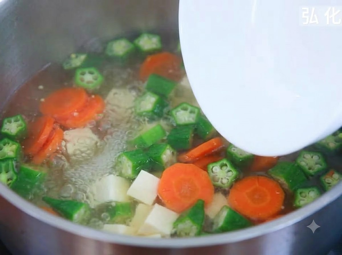 Soft tofu cubes being added from a plate into a bubbling pot of vegetable soup.