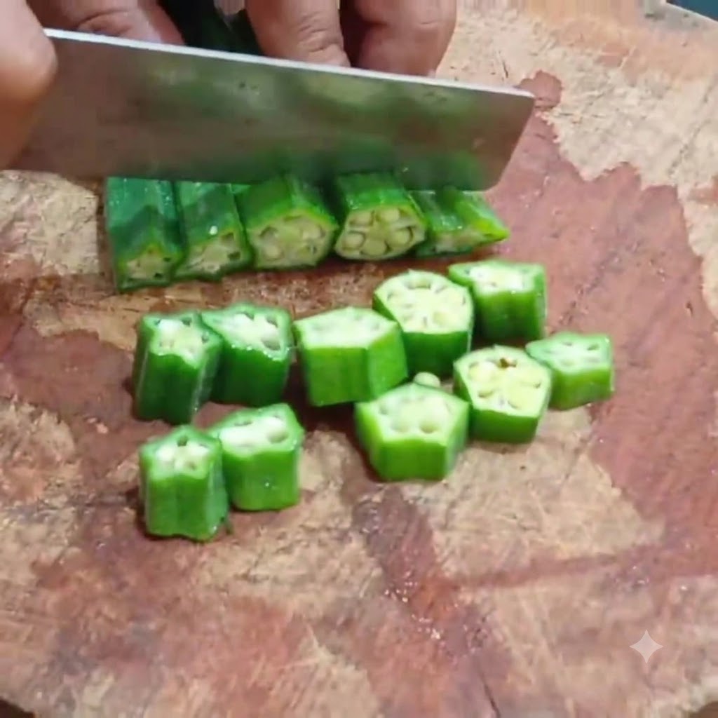A kitchen knife cutting blanched okra into even round slices on a wooden cutting board.