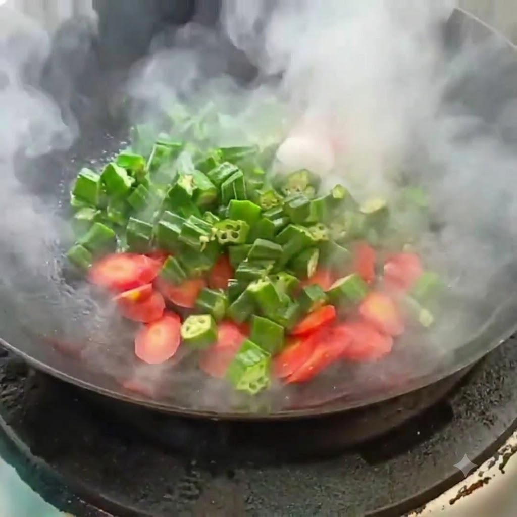 Sliced okra and carrot being stir-fried in a hot wok with rising steam.