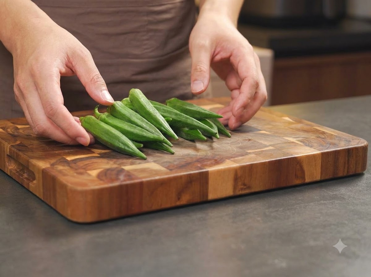 Hands rubbing salt onto fresh whole green okra pods arranged on a cutting board.