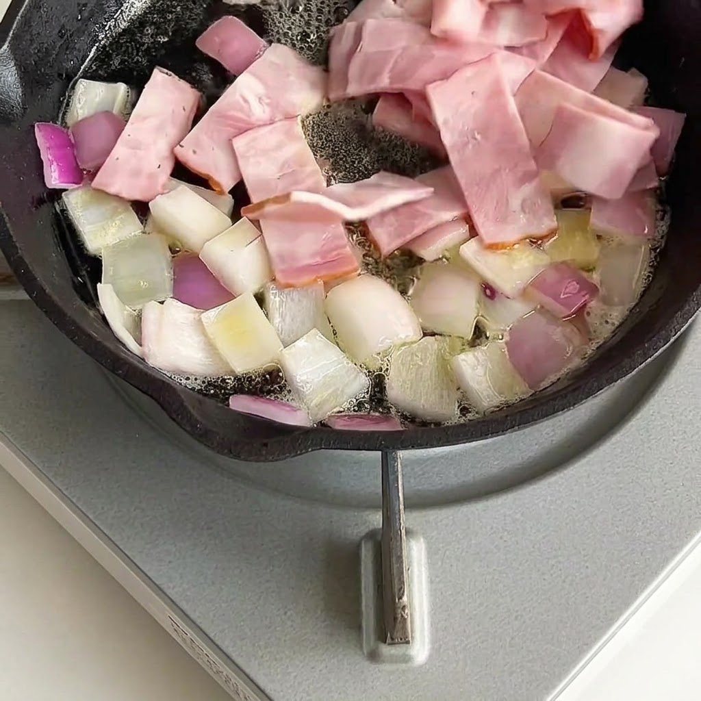 Bacon pieces mixed and stir-fried with onions in the skillet.