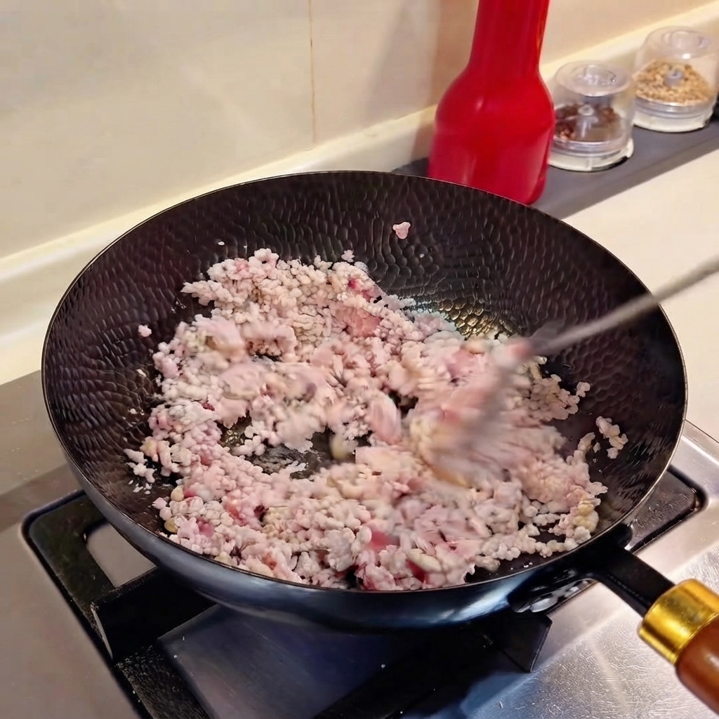 Chopped scallions and minced garlic being tossed with minced meat in a wok.