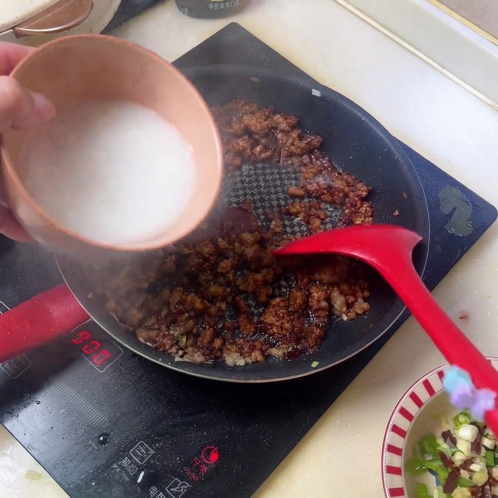 White starch water being poured from a bowl into the pan of dark minced meat sauce.