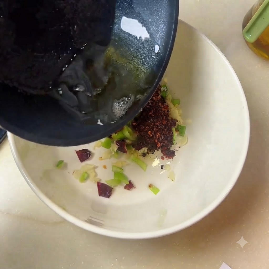 Hot oil streaming from a pan into a white bowl filled with spices and aromatics.