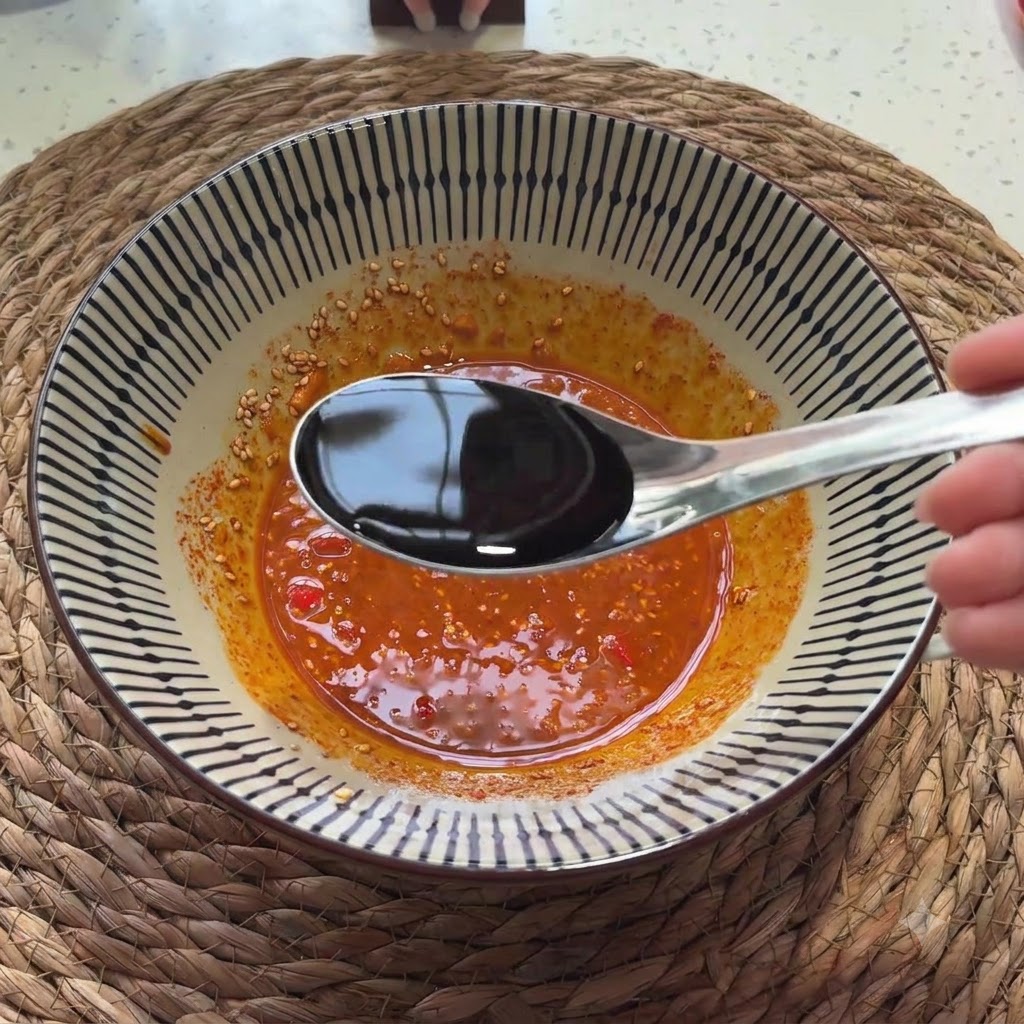 Light soy sauce being poured from a spoon into the seasoned sauce mixture.