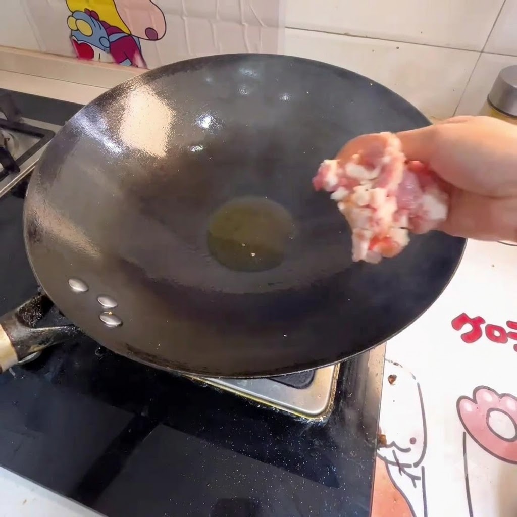 Hand dropping minced meat into a wok with hot oil.