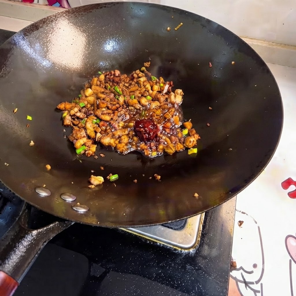 Bean paste dollop placed among stir-fried meat in the wok.