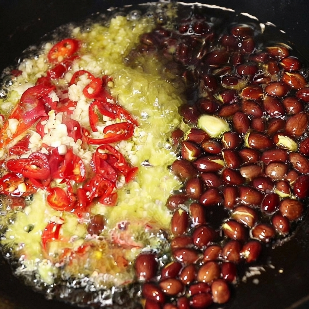 Minced garlic, sliced red chilies, and whole peanuts sizzling in hot oil inside a wok.