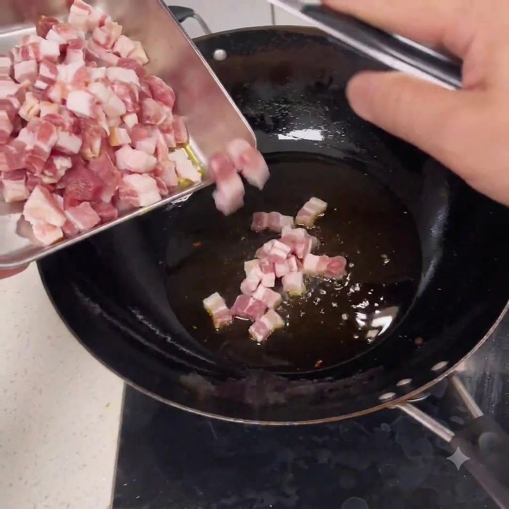 Raw diced pork pieces sliding from a metal tray into a wok with hot oil.