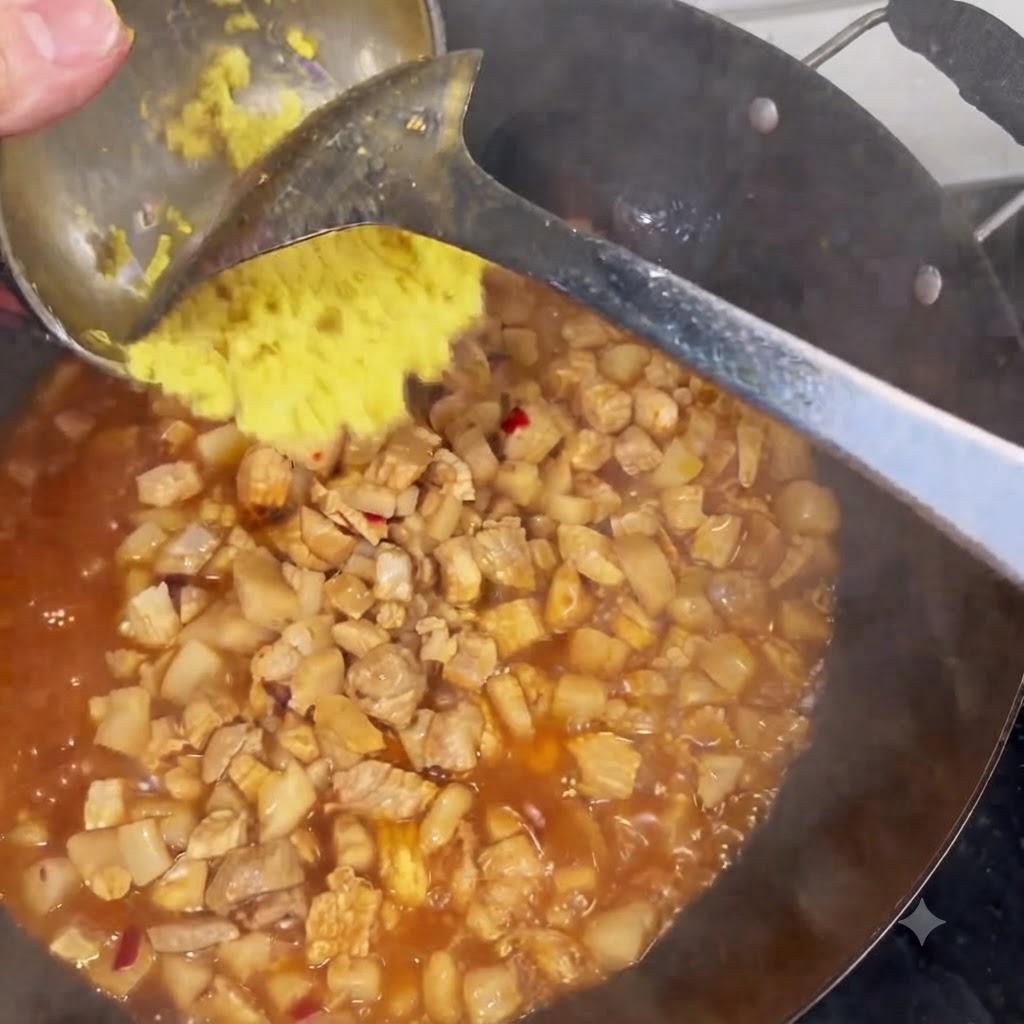 Minced ginger being scraped from a ladle into a wok filled with simmering meat and sauce.