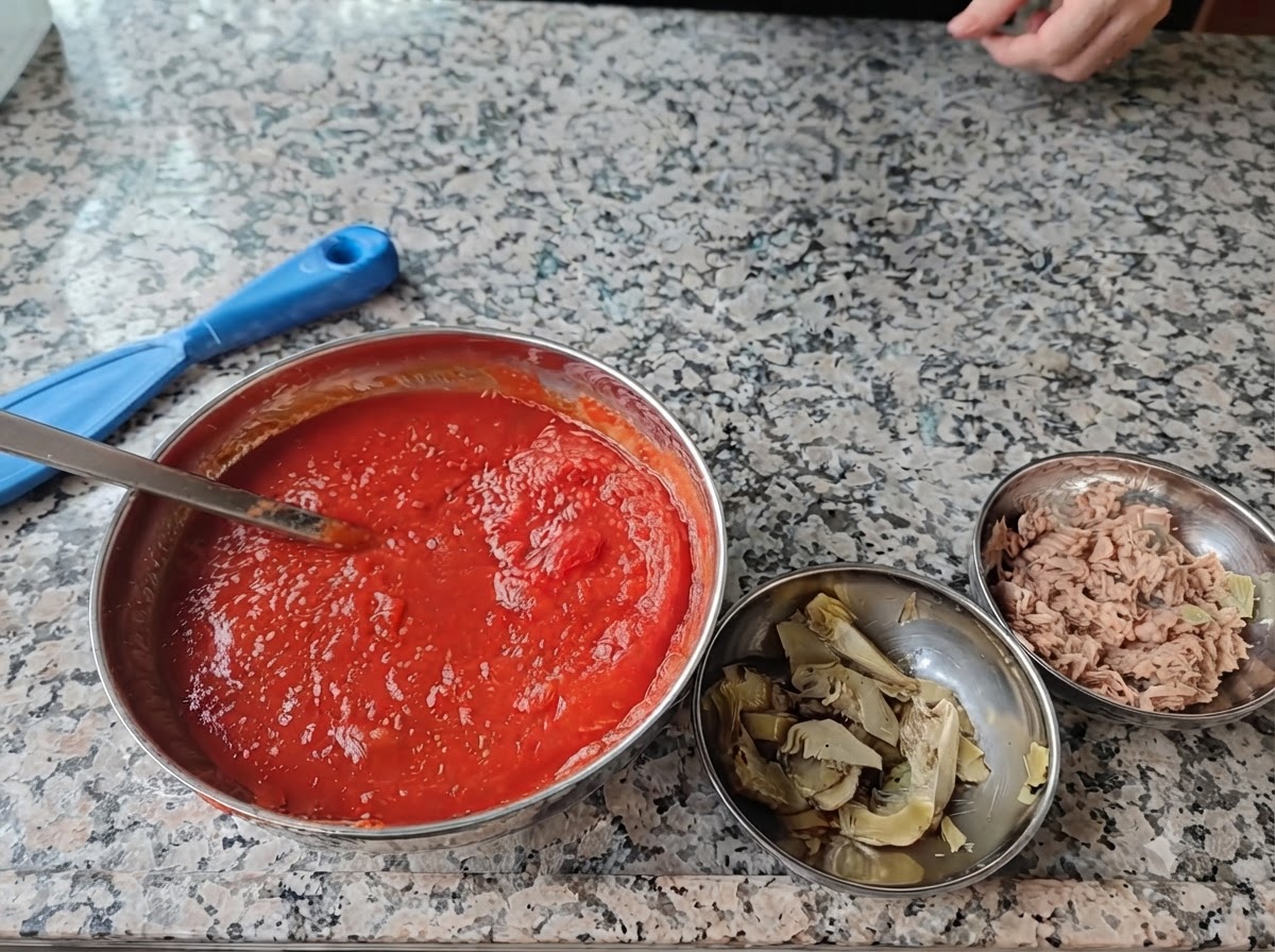 Four steel bowls filled with pizza ingredients arranged on a marble surface.