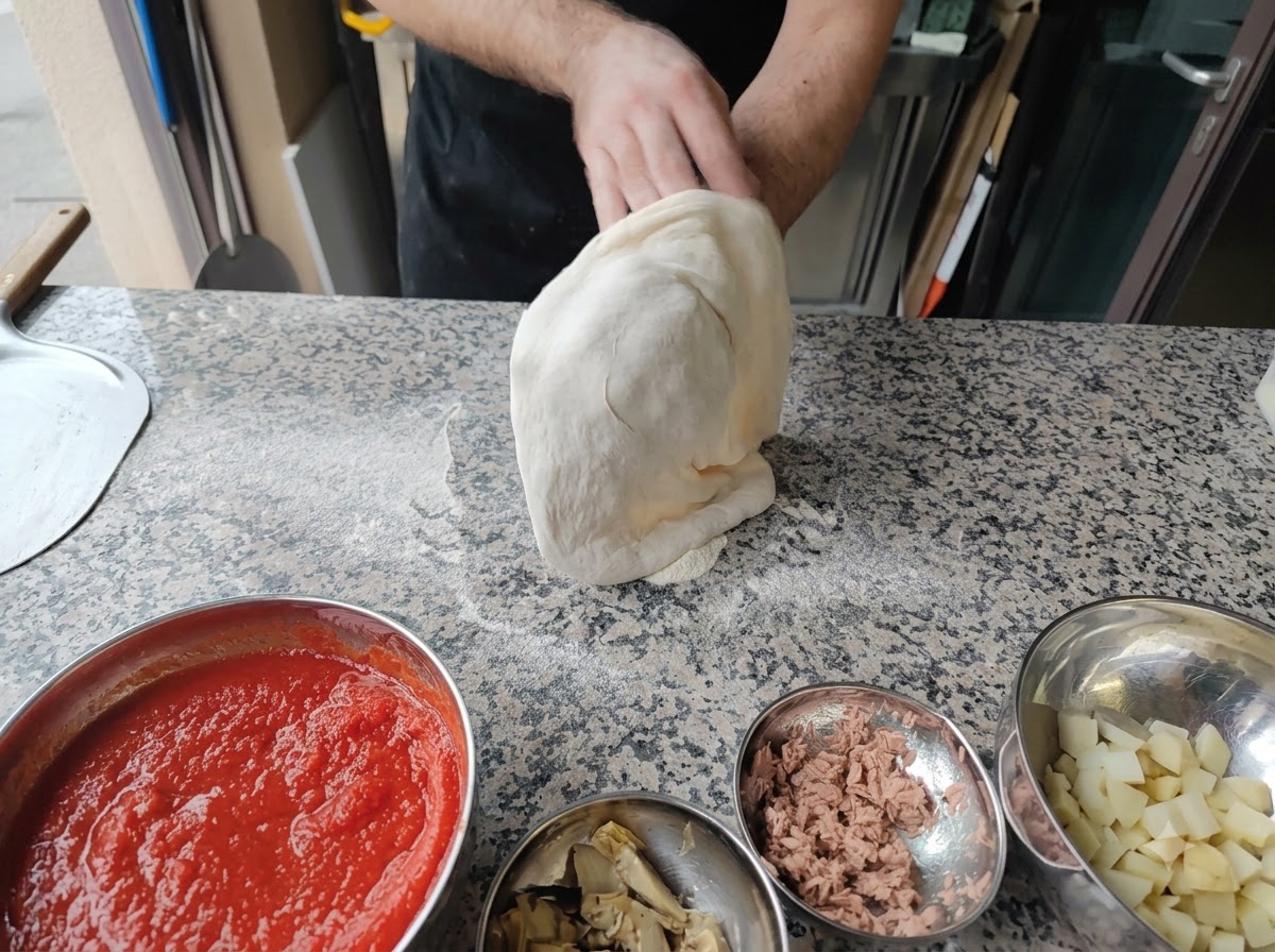 A person stretching pizza dough over their fists in the air.