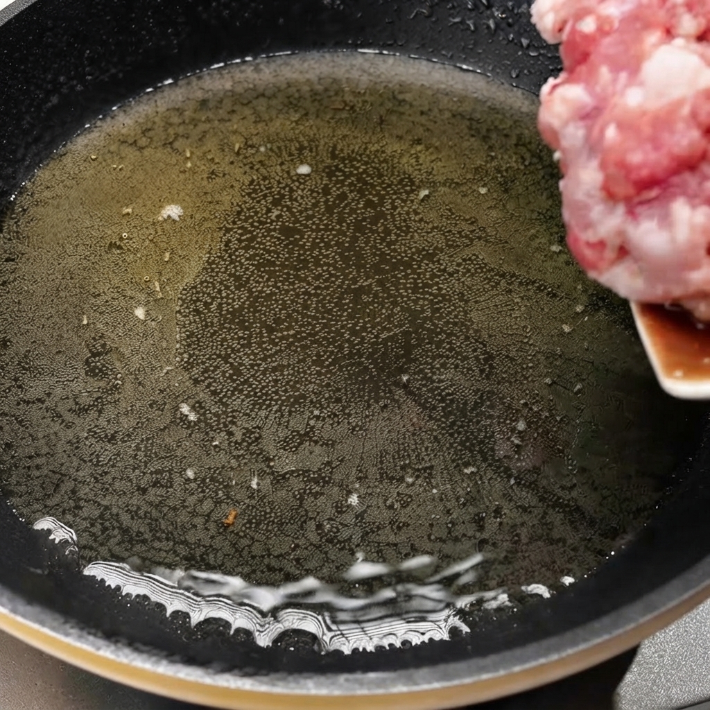 Minced pork being transferred into a hot skillet with oil to begin cooking.