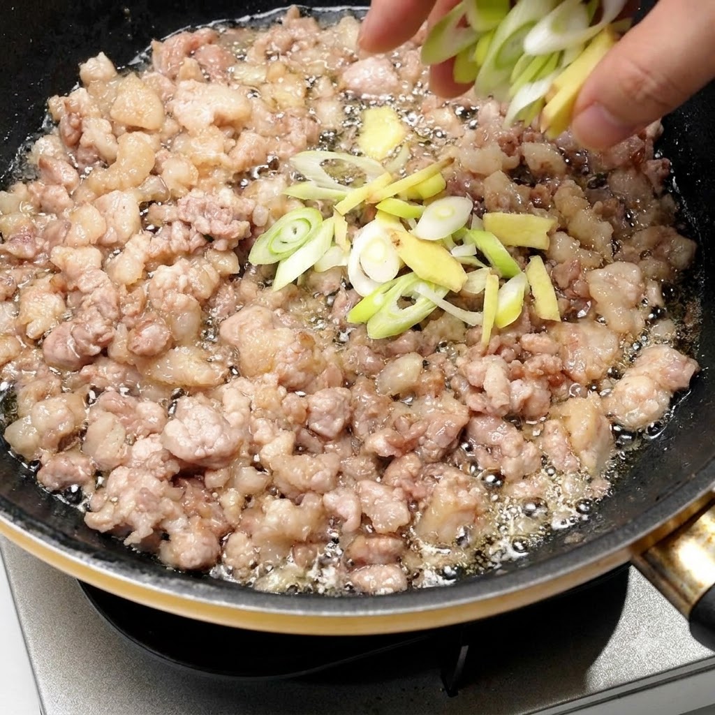 Chopped scallions and ginger being added directly into the skillet with browned minced pork.
